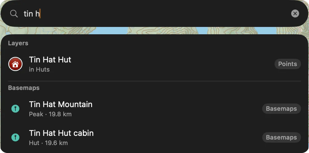 The search bar on Mac with tin h typed and its results below: a Layers section listing Tin Hat Hut, then a Basemaps section listing Tin Hat Mountain and Tin Hat Hut cabin with their distances